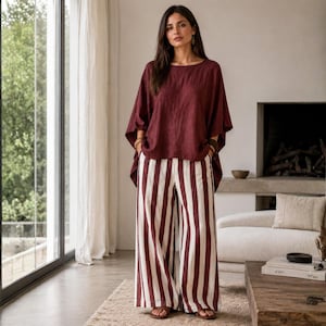 May include: A dark maroon short-sleeved top with a wide, loose fit paired with high-waisted, wide-leg trousers featuring vertical stripes in alternating maroon and off-white colors. The outfit is worn with simple brown sandals.