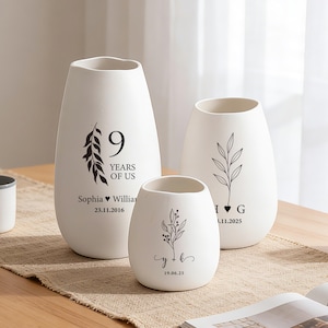 May include: Three white ceramic vases with matte finishes and black printed designs. The largest vase features a leaf graphic, the text 9 YEARS OF US, Sophia, William, and 23.11.2016. The others display leaf illustrations, initials, and dates.