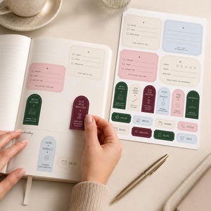 May include: A sticker sheet featuring various rectangular and arched labels in muted tones of pink, blue, green, and cream. The stickers include text prompts like "Water," "Food," "Begin Anyway," and "Just Five Minutes," designed for planner organization.