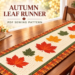 Puede incluir: Un camino de mesa rectangular con un centro color crema y aplicaciones de hojas de arce acolchadas en rojo, naranja y verde. El borde consta de una tira de tela verde y una tela de cuadros multicolor. El texto dice AUTUMN LEAF RUNNER PDF SEWING PATTERN.