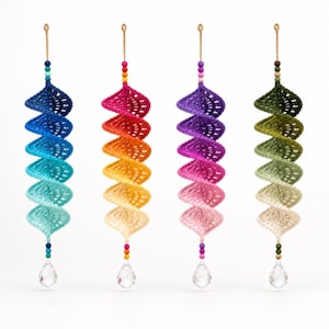May include: Four spiral-shaped crochet ornaments hanging vertically. Each features a gradient color scheme: blue, warm sunset tones, purple to pink, and green to cream. They are topped with a loop and finished with colorful beads and a clear crystal.