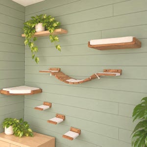 May include: A wall-mounted cat furniture set featuring a wooden bridge, several rectangular shelves with white cushions, and a corner shelf. The natural wood finish contrasts with the white fabric pads, creating a multi-level climbing system.