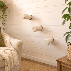 May include: Three cylindrical wall-mounted cat perches with a light beige sisal rope covering and dark wood circular end caps, arranged in a staggered diagonal pattern on a white horizontal plank wall to provide elevated climbing surfaces.