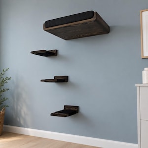 May include: A set of four wall-mounted floating shelves made of dark stained wood with visible grain. Each shelf features a rectangular black fabric cushion on the top surface, providing a soft platform for each of the four tiered wooden levels.