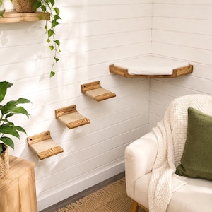 May include: A set of wall-mounted cat furniture consisting of three small rectangular wooden steps with beige fabric inserts and one larger triangular corner platform featuring a white cushion, all attached to a white horizontal paneled wall.