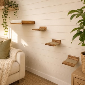 May include: A set of four wall-mounted wooden cat shelves arranged in a staggered pattern. Each shelf features a natural wood grain finish and a soft, light-colored fabric pad on the top surface for resting, providing a functional climbing structure.