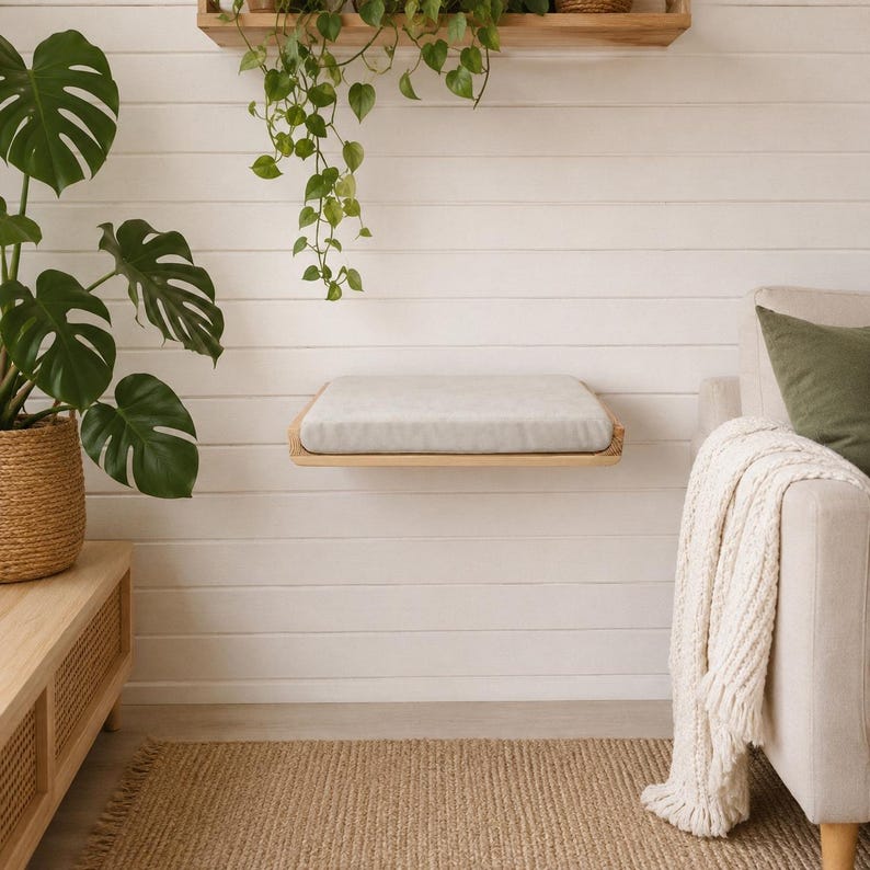 Wall mounted natural wood cat bed with a soft white cushion in a cozy modern living room interior.