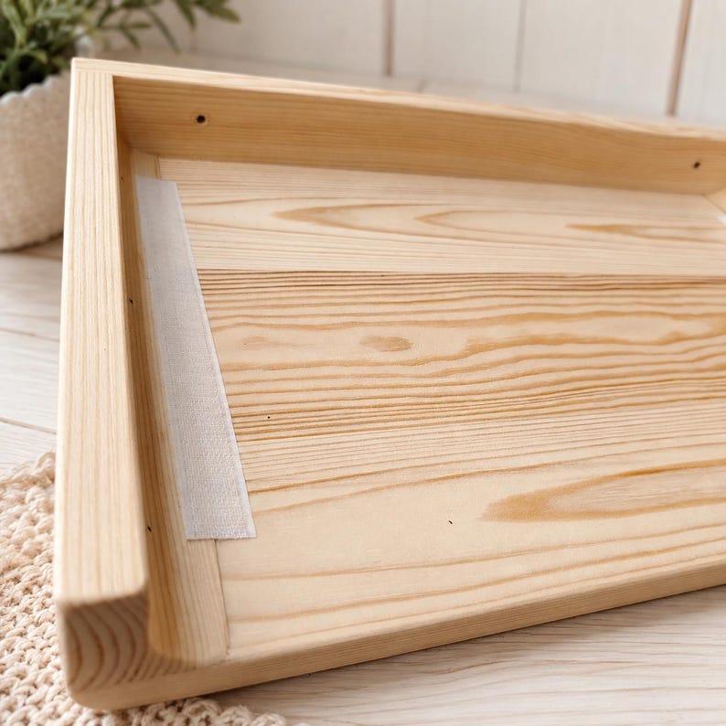 May include: A rectangular wooden tray featuring a light tan natural wood grain finish. The tray has raised sides with visible joinery and a single strip of white adhesive tape applied vertically along the interior left side of the wooden base.