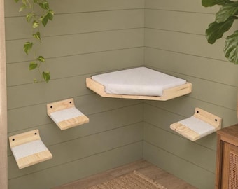 May include: A set of wall-mounted cat furniture consisting of one large corner platform and three smaller rectangular steps. Each piece is crafted from light-colored wood and features a soft, white fabric cushion for comfort and grip.