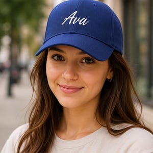 Peut inclure: Une casquette de baseball bleu roi avec le prénom Ava brodé en écriture cursive blanche sur les panneaux avant. La casquette présente une calotte structurée, une visière incurvée et des œillets cousus sur le dessus pour la ventilation.