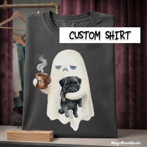 May include: A dark gray t-shirt featuring a graphic of a white ghost holding a brown mug with the text MEH and hugging a black pug dog. The shirt has a crew neckline and short sleeves. The text CUSTOM SHIRT is printed in black on a white background.