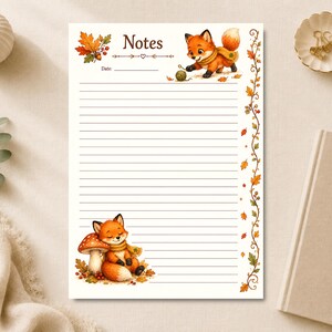 Op de afbeelding: Een rechthoekig vel gelinieerd briefpapier met het woord Notes bovenaan. Het ontwerp bevat illustraties van twee oranje vossen, herfstbladeren, bessen en een paddenstoel. Een rankenrand loopt langs de rechterkant van de pagina.