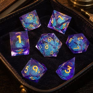 Peut inclure: Un ensemble de sept dés polyédriques composés d'une coque en résine violette translucide avec un cœur à paillettes bleu vif et des chiffres dorés. Le jeu de dés comprend diverses formes géométriques, telles qu'un d20, d12, d10, d8, d6 et d4.