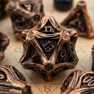 May include: A set of polyhedral dice featuring a metallic copper finish with intricate, raised branch-like detailing and dark recessed numbering. The central twenty-sided die clearly displays the numbers 11, 13, and 9 in a bold, serif font.