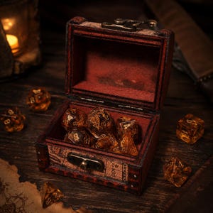 May include: A small, rectangular wooden chest with a dark red finish and a metal latch, containing several translucent amber-colored polyhedral dice with gold-colored numbers. Additional matching dice are scattered around the open chest.