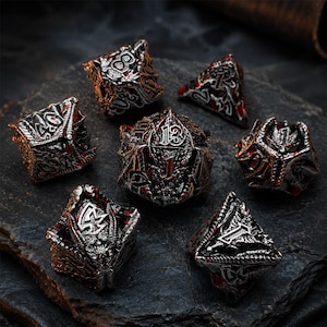 Seven-piece silver, black, and red dragon-themed metal DND dice set with raised numbers, sculpted scales, wings, and fantasy details. The polyhedral dice are arranged on a rugged dark stone slab.