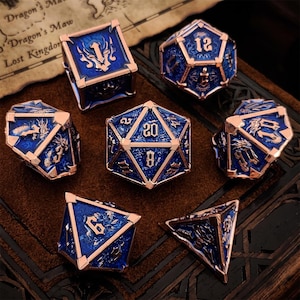 Pode incluir: Um conjunto de sete dados poliédricos com acabamento em esmalte azul profundo, molduras de metal em ouro rosa e detalhes de dragão. Cada dado exibe números em relevo numa fonte gótica, incluindo um dado de vinte faces no centro.
