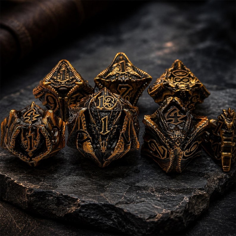 Seven-piece antique bronze and black metal DND dice set featuring raised numbers, dragon heads, wings, scales, and fantasy details. The polyhedral dice are arranged on a rugged dark stone slab.