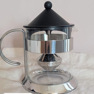 May include: A clear glass teapot with a stainless steel frame, a black conical lid with a round knob, and a metal infuser basket inside. The teapot features a curved handle and a wide base. The text "Teapot A" is printed in the bottom corner.