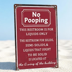 May include: A rectangular maroon metal sign with white text that reads: No Pooping, THIS RESTROOM IS FOR LIQUIDS ONLY, THE RESTROOM FOR SOLIDS, SEMI-SOLIDS, & LIQUIDS THAT OUGHT TO BE SOLID IS LOCATED AT the G wing of the building. The sign has rusted edges.