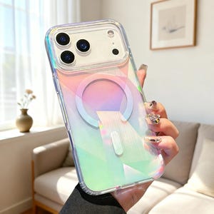 May include: A clear phone case with an iridescent, holographic geometric pattern and a circular magnetic charging ring on the back. The case features a raised camera lens protector frame and a rectangular cutout for additional magnetic accessories.
