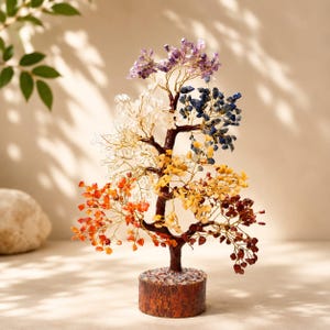 May include: A decorative tree sculpture featuring a brown trunk and base with branches made of thin gold wire. The branches are adorned with clusters of small, polished gemstones in shades of purple, blue, clear, yellow, orange, and deep red.