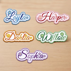 Può includere: Cinque toppe ricamate con i nomi Layla, Harper, Dahlia, Willow e Sophia. Ogni toppa presenta una combinazione di colori unica con accenti floreali abbinati, scritte in corsivo e un bordo smerlato su uno sfondo in tessuto bianco.