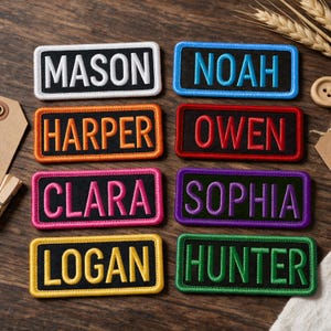 May include: Eight rectangular embroidered patches with black backgrounds and coloured borders. The patches feature the names MASON in white, NOAH in blue, HARPER in orange, OWEN in red, CLARA in pink, SOPHIA in purple, LOGAN in yellow, and HUNTER in green.