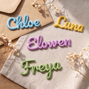 May include: Four custom name patches in cursive script. The light blue patch reads Chloe, the yellow patch reads Luna, the purple patch reads Elowen, and the light green patch reads Freya. Each patch features a raised, padded, fabric-covered texture.