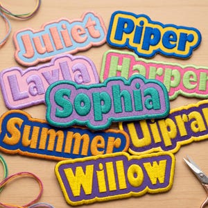 Può includere: Una collezione di toppe ricamate con nomi in vari colori, tra cui Juliet, Piper, Layla, Harper, Sophia, Summer e Willow. Ogni toppa presenta un bordo smerlato e scritte ricamate in grassetto con fili di colori contrastanti.