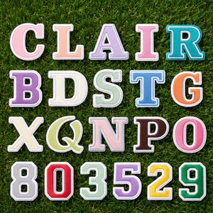 Op de afbeelding: Een verzameling opstrijkbare patches in varsity-stijl met letters en cijfers in diverse pastelkleuren en felle kleuren. Elk karakter heeft een witte rand en een textuur, waaronder de letters C, L, A, I, R, B, D, S, T, G, X, Q, N, P, O en de cijfers 8, 0, 3, 5, 2, 9.