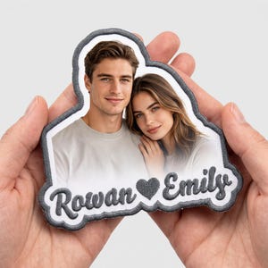 Puede incluir: Un parche bordado personalizado con un retrato fotográfico de un hombre y una mujer. El parche tiene un borde bordado en gris oscuro e incluye los nombres Rowan y Emily separados por un icono de corazón bordado en gris oscuro.