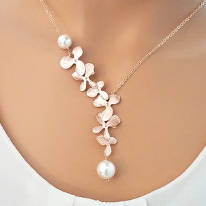 May include: A rose gold necklace with a delicate chain and a pendant featuring a cluster of small flower-shaped charms and two pearl accents.