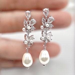 Op de afbeelding: Zilveren oorhangers met een cluster van heldere zirkonia-stenen en een enkele parel-druppel.