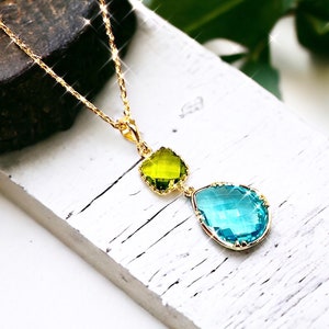 K&ouml;nnte beinhalten: Eine goldene Kettenkette mit einem tropfenf&ouml;rmigen blauen Kristallanh&auml;nger und einem kleineren quadratischen gr&uuml;nen Kristallanh&auml;nger.