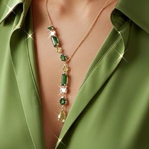 May include: A gold-toned lariat necklace featuring a vertical drop design with alternating emerald green rectangular and square-cut stones, interspersed with smaller clear faceted crystals, suspended from a delicate gold-toned chain.