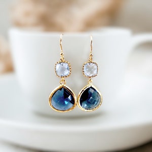 May include: Gold earrings with a teardrop-shaped blue gemstone and a smaller square clear gemstone.