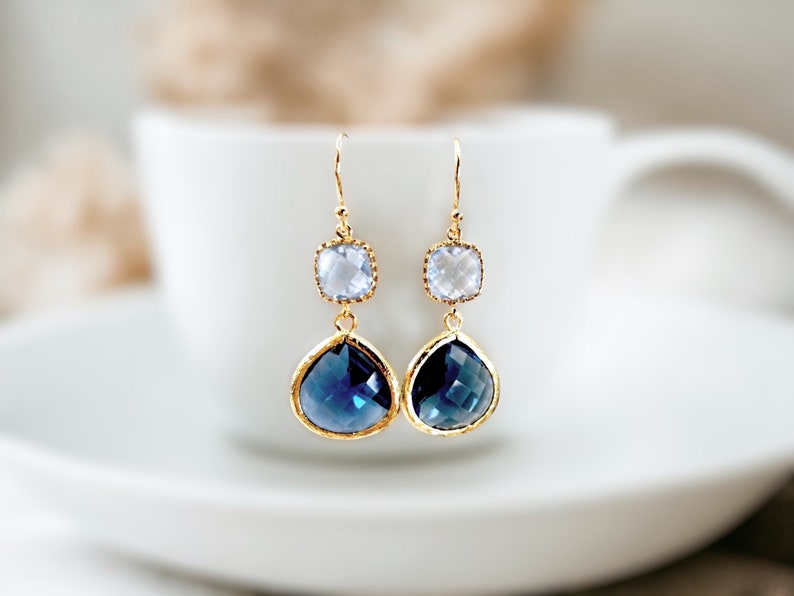 May include: Gold earrings with a teardrop-shaped blue gemstone and a smaller square clear gemstone.