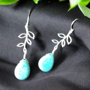 May include: Silver earrings with a delicate branch design and turquoise teardrop-shaped stones.