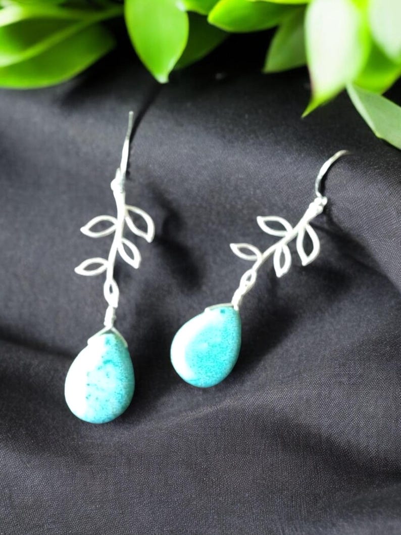 May include: Silver earrings with a delicate branch design and turquoise teardrop-shaped stones.