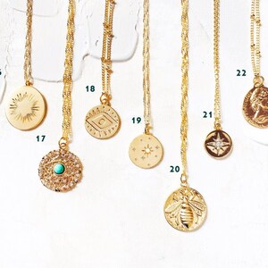 May include: Ten gold necklaces with different pendants, including a sun, an eye, a crescent moon, a star, a compass, a bee, and a profile of a woman. The necklaces are displayed on a white background.