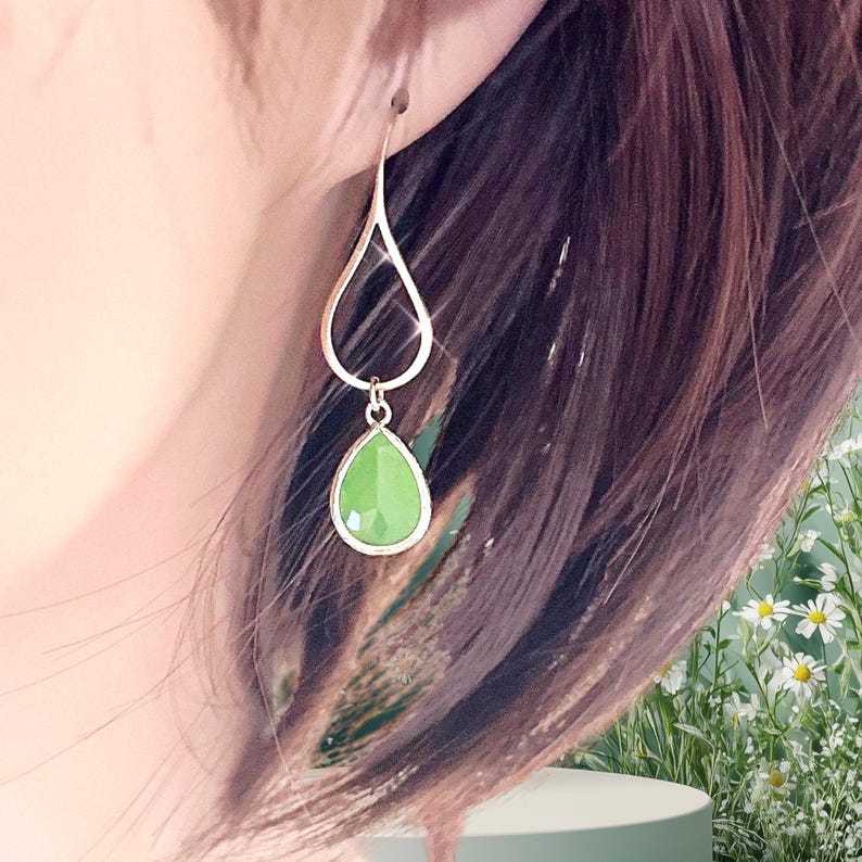 Puede incluir: Un par de pendientes colgantes con una piedra preciosa verde en forma de l&aacute;grima que cuelga de un marco dorado en forma de l&aacute;grima.