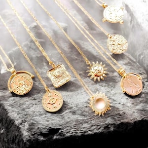 May include: A set of eight gold-toned necklaces with various pendant designs, including a sun, an eye, and a square. The necklaces are displayed on a gray textured surface.