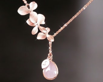 May include: A delicate rose gold necklace with a teardrop-shaped pink stone pendant. The necklace features three small flower charms.