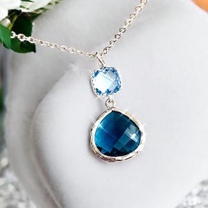 May include: A silver chain necklace with a teardrop-shaped blue crystal pendant and a smaller square blue crystal above it.