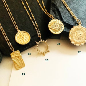 May include: Five gold necklaces with different pendants. The pendants include a sun, a flower, a face, an eye, and a religious symbol. The necklaces are on a dark background.