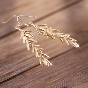 Könnte beinhalten: Ein Paar goldfarbene Ohrringe mit einem zarten Blattdesign. Die Ohrringe sind im Hänge-Stil und haben einen Cluster aus kleinen, blattartigen Anhängern.
