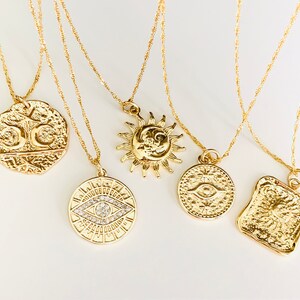 May include: Five gold necklaces with different pendants. The pendants are a sun and moon, an eye with a crystal, a square with a sun, and two different coins.