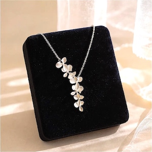 May include: A silver-colored necklace featuring a floral design. The pendant showcases a cascade of delicate flower-shaped elements, suspended from a fine chain. The necklace is displayed on a black velvet surface.