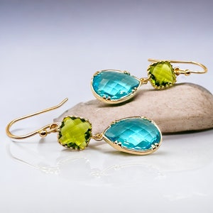 K&ouml;nnte beinhalten: Goldene Ohrh&auml;nger mit einem tropfenf&ouml;rmigen blauen Edelstein und einem quadratischen gr&uuml;nen Edelstein.